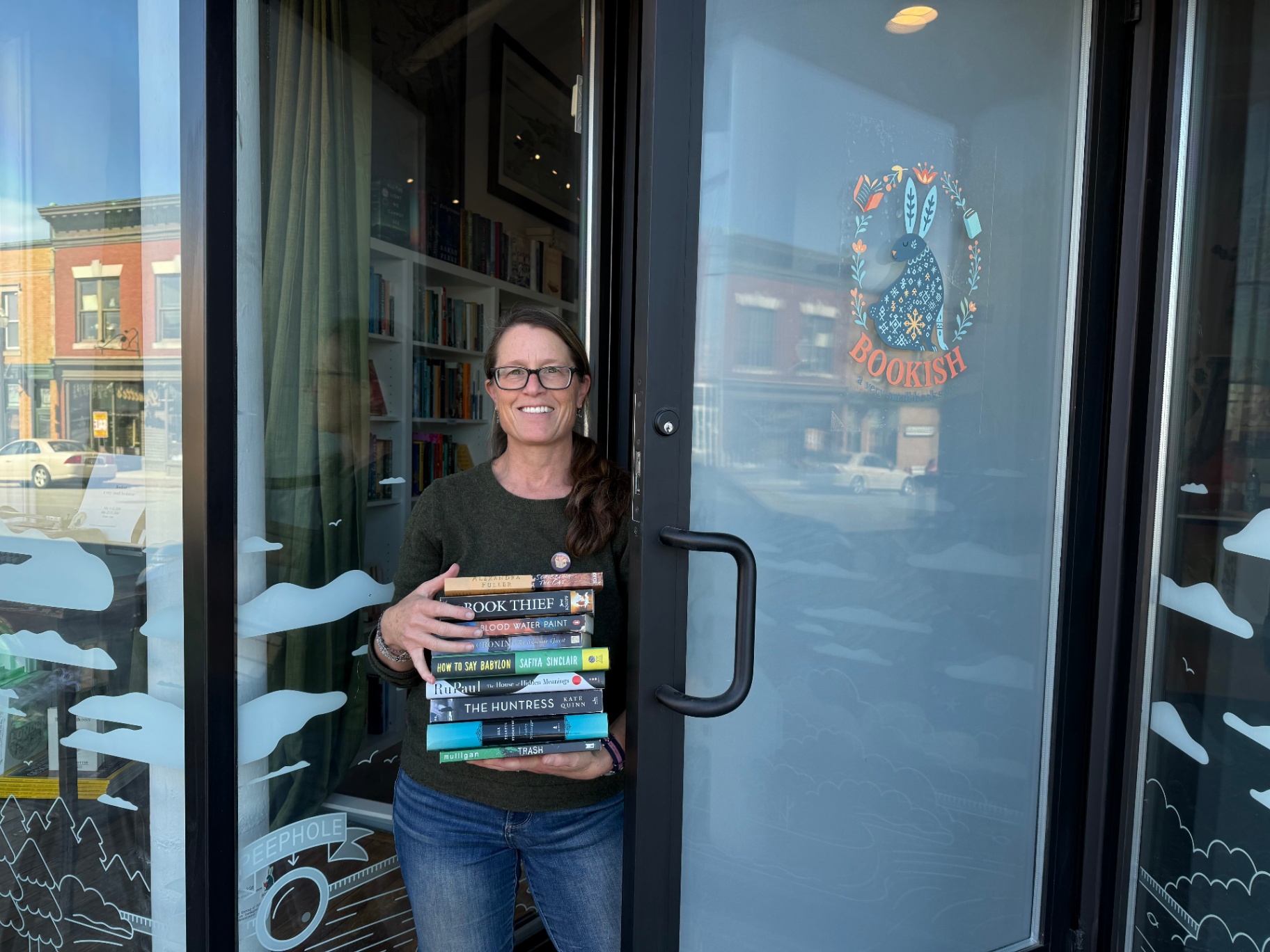 Bookish owner at the shop door with the folk-art rabbit logo on the glass